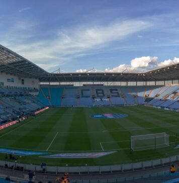 Wide view across the pitch and sky-blue stands at Coventry Building Society Arena