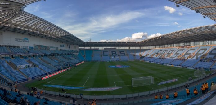 Wide view across the pitch and sky-blue stands at Coventry Building Society Arena